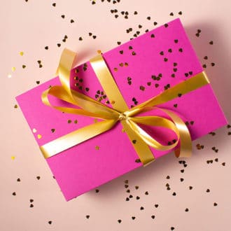 pink gift box with gold ribbon and confetti