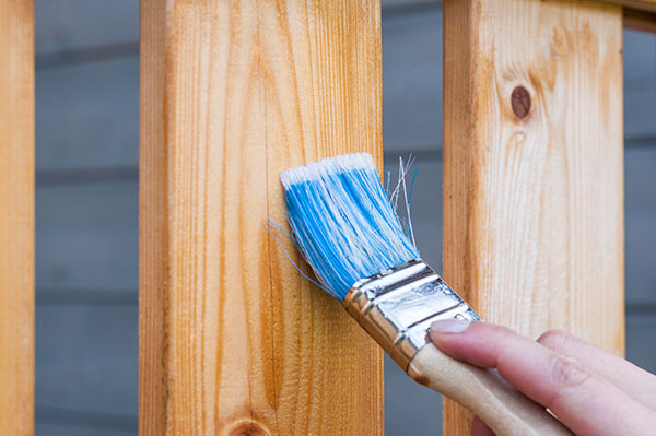 Painting wooden fence with large paintbrush