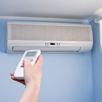 Person turning on split air conditioner unit with remote