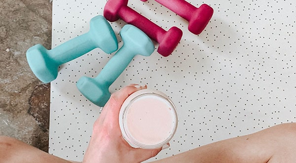 person holding smoothie with gym weights