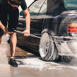 Man using high pressure cleaning machine to wash car tyres