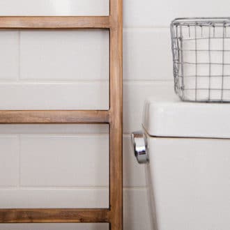 white tiled bathroom with white toilet and mesh basket and wooden ladder