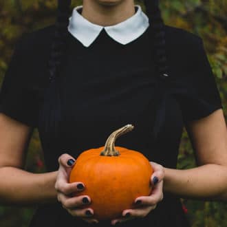 adult Wednesday Adams halloween costume blck dress with hands holding pumpkin