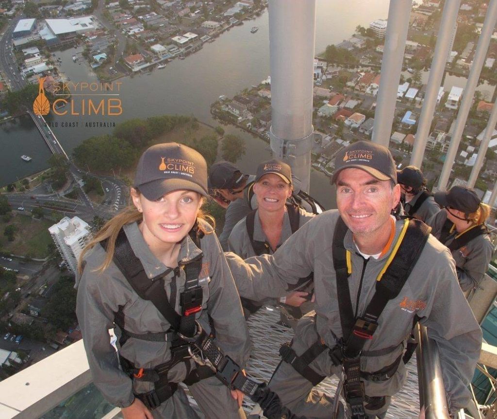 Three people looking at the camera strapped in wearing grey on standing on stairs of the Q1 sky point climb