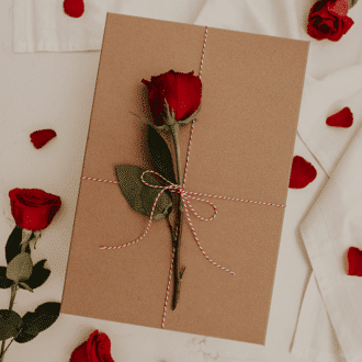 Rose laying on a square gift wrapped in brown paper